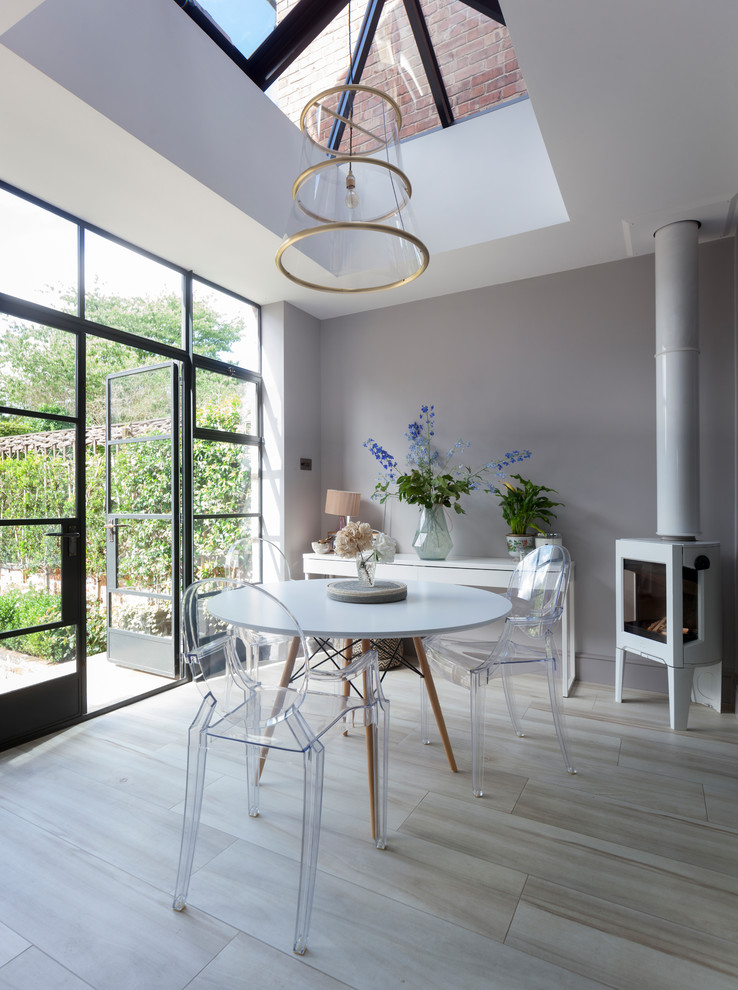 Industrial open plan dining in Cheshire with grey walls, porcelain floors, a wood stove and beige floor.