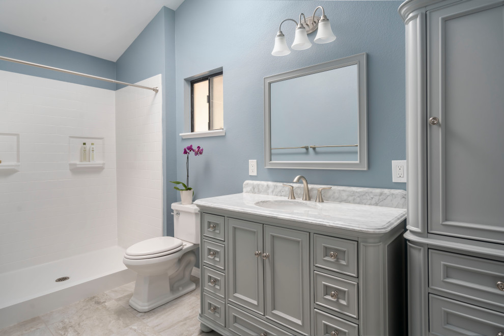 This is an example of a mid-sized 3/4 bathroom in Los Angeles with furniture-like cabinets, grey cabinets, an alcove shower, a two-piece toilet, blue walls, ceramic floors, an undermount sink, marble benchtops, grey floor, a shower curtain, grey benchtops, a single vanity and a freestanding vanity.