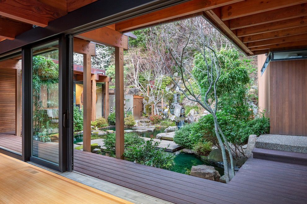 This is an example of a large asian backyard patio in Other with a water feature, decking and an awning.