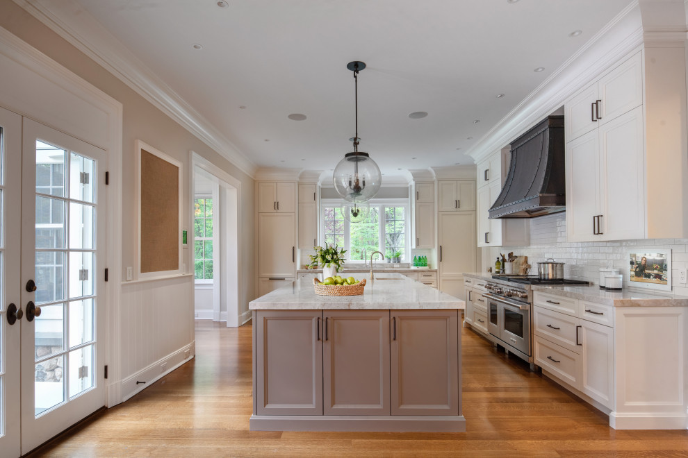 This is an example of a transitional l-shaped kitchen in New York with recessed-panel cabinets, white cabinets, white splashback, subway tile splashback, stainless steel appliances, medium hardwood floors, with island, brown floor and grey benchtop.