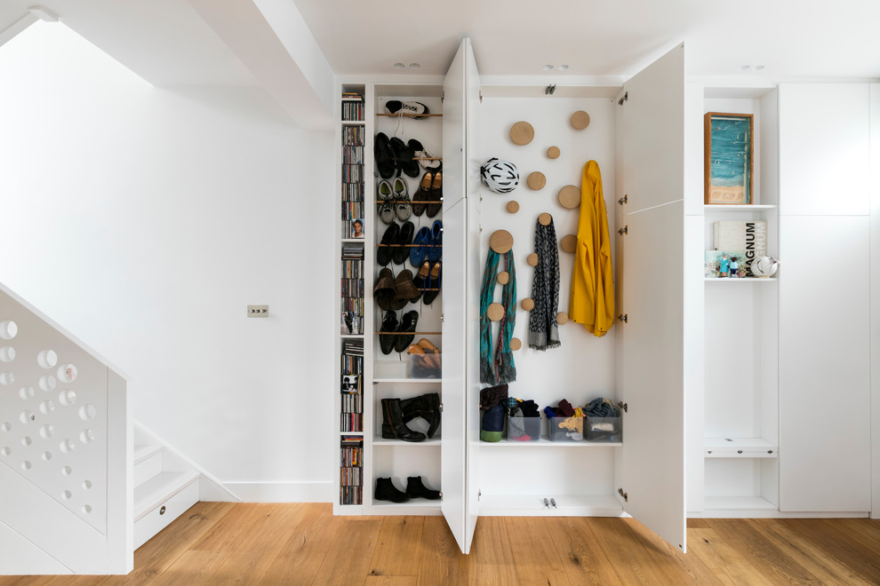 Photo of a contemporary gender-neutral built-in wardrobe in London with white cabinets and medium hardwood floors.