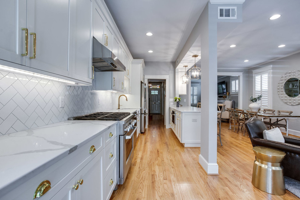 Example of a mid-sized transitional galley light wood floor and beige floor eat-in kitchen design in DC Metro with a farmhouse sink, shaker cabinets, white cabinets, quartz countertops, white backsplash, subway tile backsplash, stainless steel appliances, a peninsula and white countertops