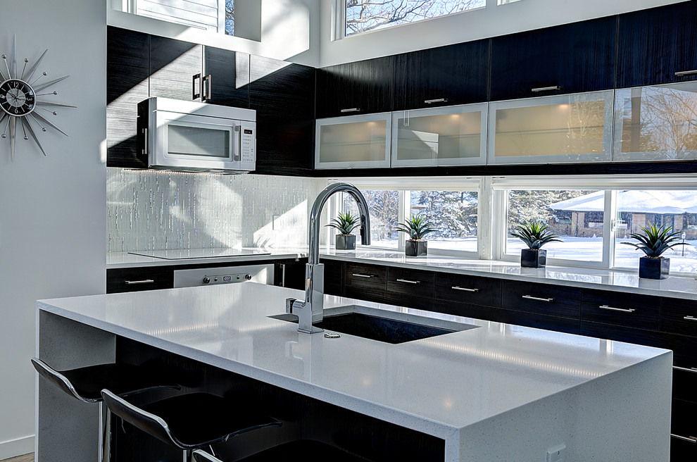 Photo of a mid-sized contemporary l-shaped open plan kitchen in Grand Rapids with an undermount sink, quartz benchtops, white appliances, with island, black cabinets, white splashback, glass tile splashback, light hardwood floors and flat-panel cabinets.