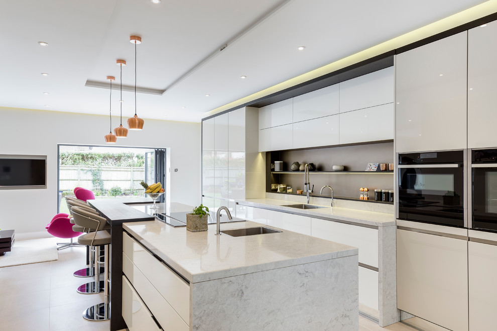 This is an example of a contemporary galley open plan kitchen in London with an undermount sink, flat-panel cabinets, white cabinets, stainless steel appliances and with island.