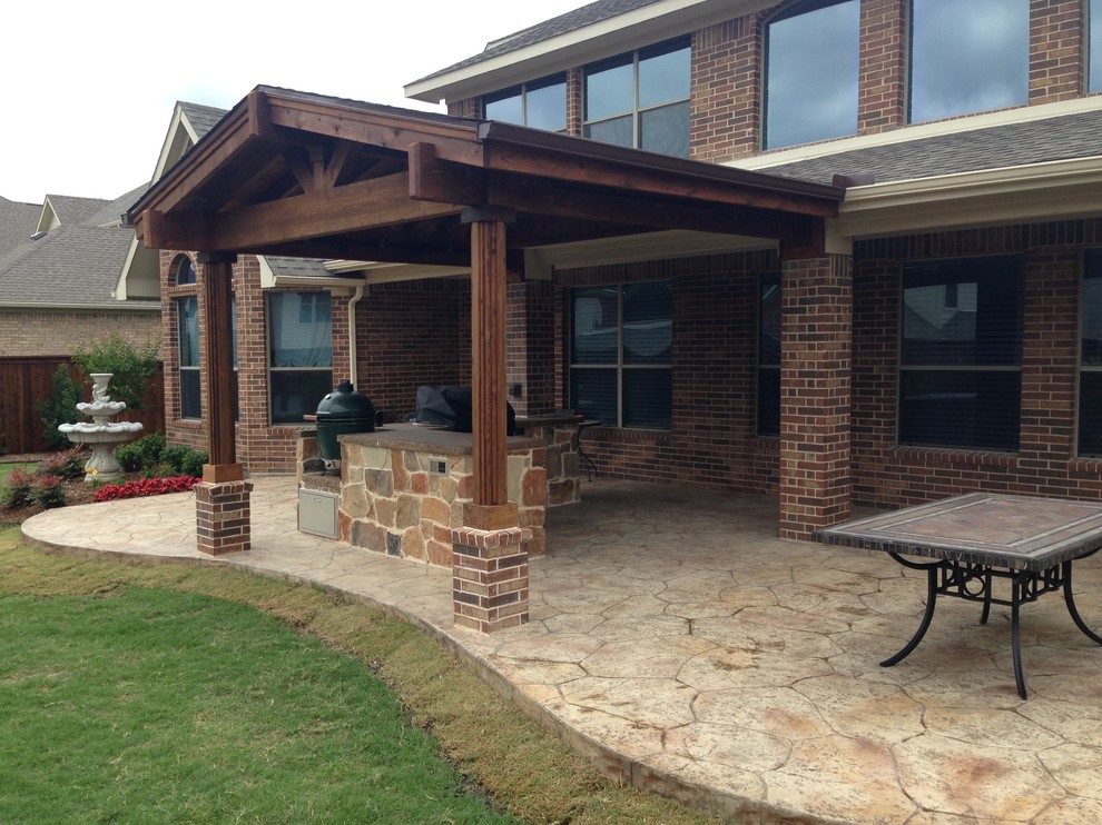 This is an example of a mid-sized country backyard patio in Dallas with an outdoor kitchen, stamped concrete and an awning.