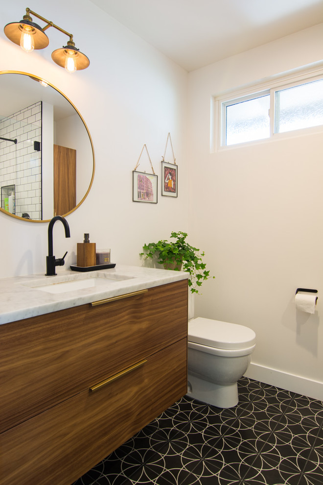 Inspiration for a mid-sized eclectic master bathroom in San Francisco with flat-panel cabinets, medium wood cabinets, an open shower, a one-piece toilet, white tile, porcelain tile, white walls, cement tiles, a drop-in sink, marble benchtops, black floor, a hinged shower door and grey benchtops.