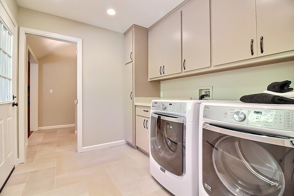 Photo of a mid-sized traditional single-wall utility room in San Francisco with flat-panel cabinets, grey cabinets, solid surface benchtops, beige walls, travertine floors and a side-by-side washer and dryer.