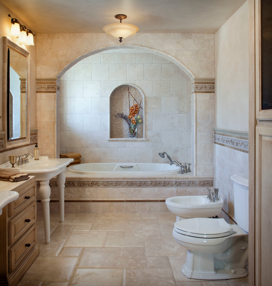 This is an example of a mediterranean bathroom in Los Angeles with raised-panel cabinets, light wood cabinets, marble benchtops, a hot tub, a bidet, beige tile, stone tile and a pedestal sink.