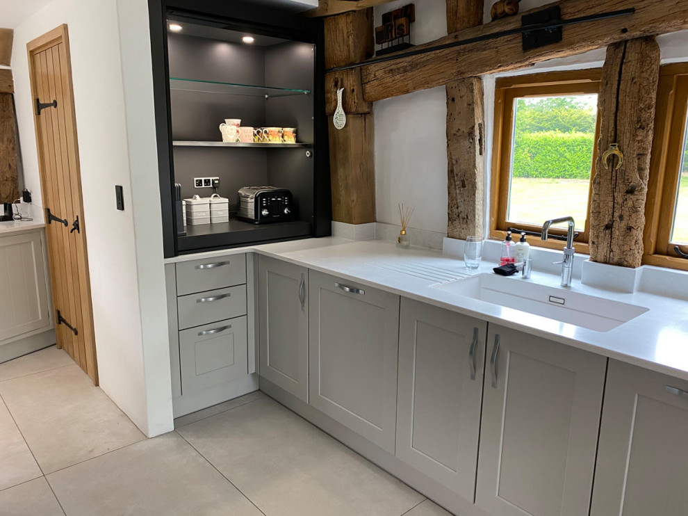 Inspiration for a large country l-shaped open plan kitchen in Essex with an integrated sink, shaker cabinets, grey cabinets, quartz benchtops, white splashback, black appliances, ceramic floors, with island, white floor and white benchtop.