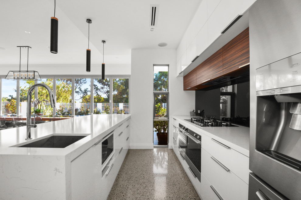 Photo of a contemporary galley kitchen in Perth with an undermount sink, flat-panel cabinets, white cabinets, black splashback, stainless steel appliances, concrete floors, with island, grey floor and white benchtop.