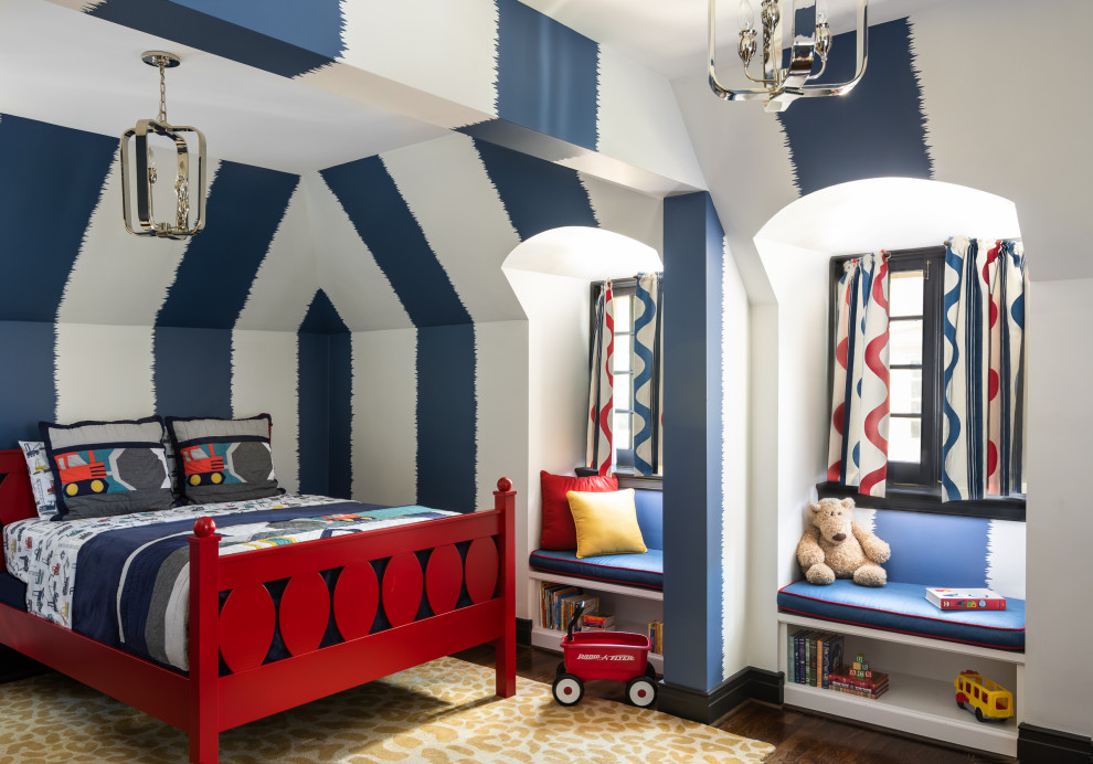 Boy's Bedroom - A long-term client was expecting her third child. Alas, this meant that baby number two was getting booted from the coveted nursery as his sister before him had. The most convenient room in the house for the son, was dad’s home office, and dad would be relocated into the garage carriage house. 
For the new bedroom, mom requested a bold, colorful space with a truck theme.
The existing office had no door and was located at the end of a long dark hallway that had been painted black by the last homeowners. First order of business was to lighten the hall and create a wall space for functioning doors. The awkward architecture of the room with 3 alcove windows, slanted ceilings and built-in bookcases proved an inconvenient location for furniture placement. We opted to place the bed close the wall so the two-year-old wouldn’t fall out. The solid wood bed and nightstand were constructed in the US and painted in vibrant shades to match the bedding and roman shades. The amazing irregular wall stripes were inherited from the previous homeowner but were also black and proved too dark for a toddler. Both myself and the client loved them and decided to have them re-painted in a daring blue. The daring fabric used on the windows counter- balance the wall stripes.
Window seats and a built-in toy storage were constructed to make use of the alcove windows. Now, the room is not only fun and bright, but  functional.