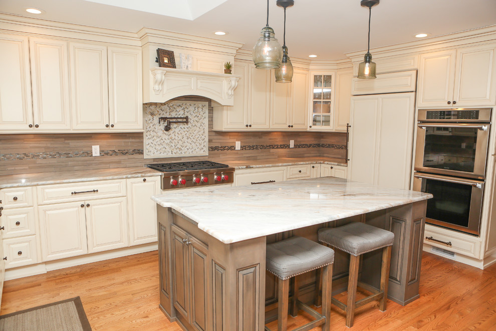 Inspiration for a large transitional u-shaped light wood floor eat-in kitchen remodel in Newark with an undermount sink, raised-panel cabinets, distressed cabinets, granite countertops, brown backsplash, mosaic tile backsplash, stainless steel appliances and an island