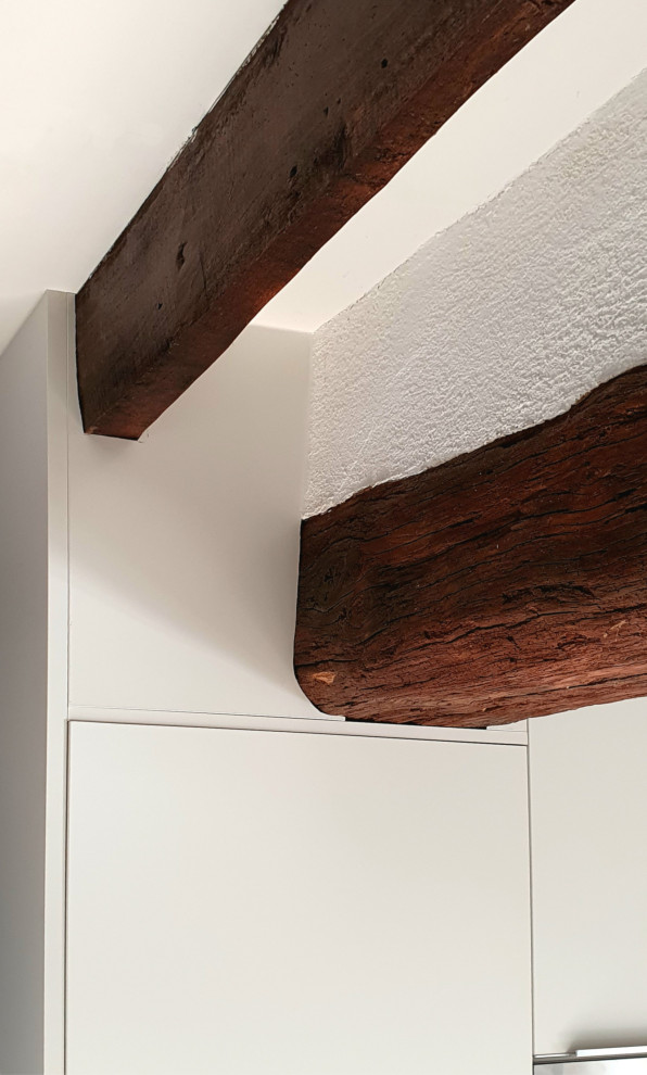 Cette image montre une grande cuisine ouverte encastrable et blanche et bois design en L avec un évier intégré, un placard à porte plane, des portes de placard blanches, un plan de travail en bois, une crédence marron, une crédence en bois, un sol en carrelage de céramique, îlot, un sol beige, un plan de travail marron et poutres apparentes.