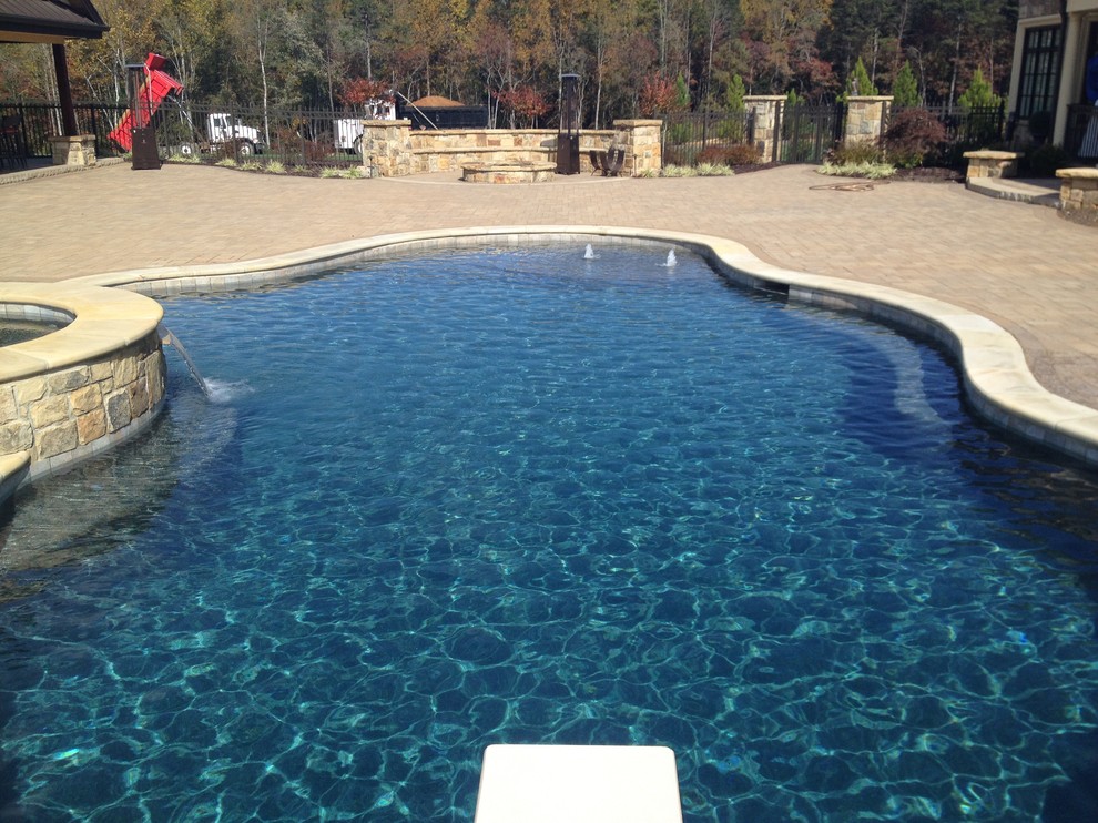 Large mediterranean backyard custom-shaped natural pool in Raleigh with a water feature and concrete pavers.