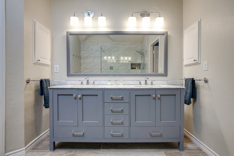 This is an example of a large contemporary master bathroom in Dallas with shaker cabinets, grey cabinets, an open shower, white tile, porcelain tile, beige walls, porcelain floors, an undermount sink, marble benchtops, brown floor, an open shower and white benchtops.