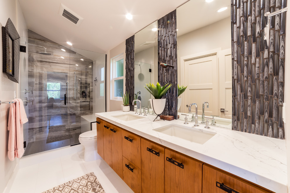 Inspiration for a large midcentury master bathroom in San Diego with shaker cabinets, medium wood cabinets, a curbless shower, a two-piece toilet, brown tile, glass sheet wall, white walls, ceramic floors, an undermount sink, granite benchtops, white floor, a hinged shower door and white benchtops.