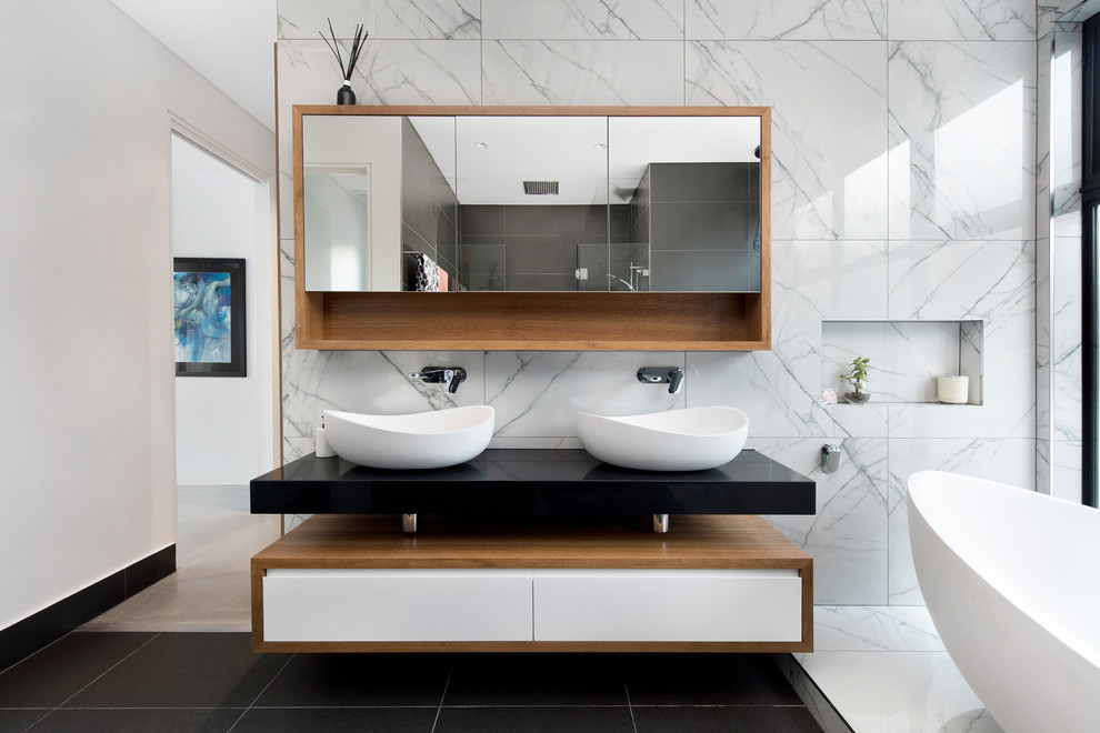 Design ideas for a contemporary bathroom in Canberra - Queanbeyan with flat-panel cabinets, white cabinets, a freestanding tub, white tile, white walls, a vessel sink, black floor and black benchtops.