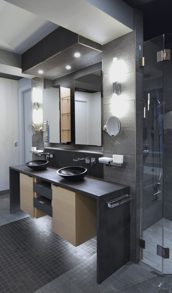 This is an example of a mid-sized modern master bathroom in Charlotte with flat-panel cabinets, light wood cabinets, a freestanding tub, a curbless shower, gray tile, porcelain tile, white walls, porcelain floors, a vessel sink, engineered quartz benchtops, grey floor, a hinged shower door, grey benchtops, an enclosed toilet, a double vanity, a floating vanity and coffered.