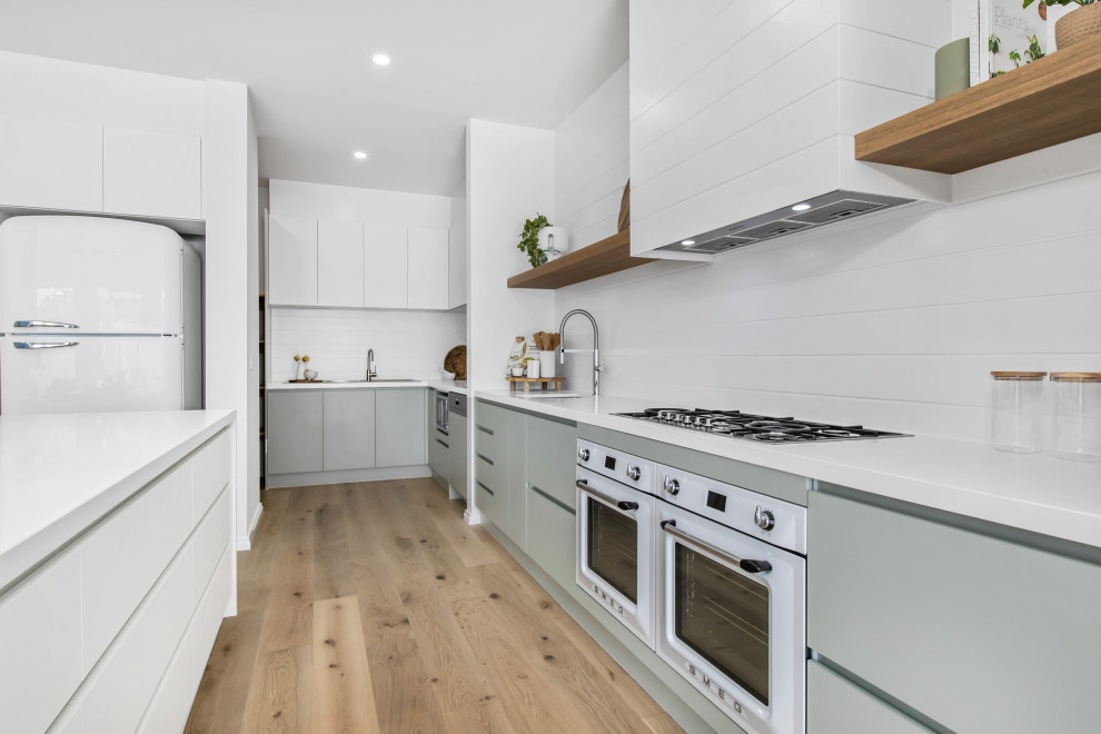 Inspiration for a contemporary single-wall eat-in kitchen in Melbourne with an undermount sink, white splashback, stainless steel appliances, with island, white benchtop and vaulted.