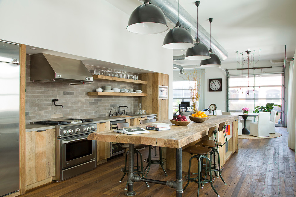 This is an example of a large industrial galley open plan kitchen in Los Angeles with flat-panel cabinets, with island, wood benchtops, grey splashback, stainless steel appliances, light wood cabinets and dark hardwood floors.