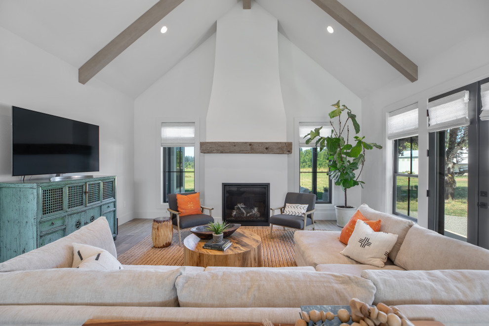 Expansive country open concept living room in Portland with a library, white walls, vinyl floors, a standard fireplace, a plaster fireplace surround, a freestanding tv, brown floor and exposed beam.