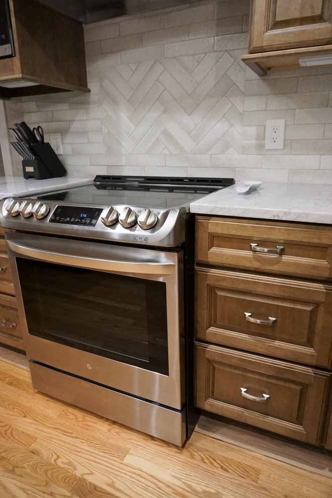 Eat-in kitchen - mid-sized traditional l-shaped light wood floor eat-in kitchen idea in Providence with a farmhouse sink, raised-panel cabinets, brown cabinets, quartzite countertops, beige backsplash, subway tile backsplash, stainless steel appliances, an island and multicolored countertops
