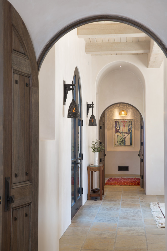 This is an example of a small mediterranean hallway in Santa Barbara with white walls, limestone floors and beige floor.