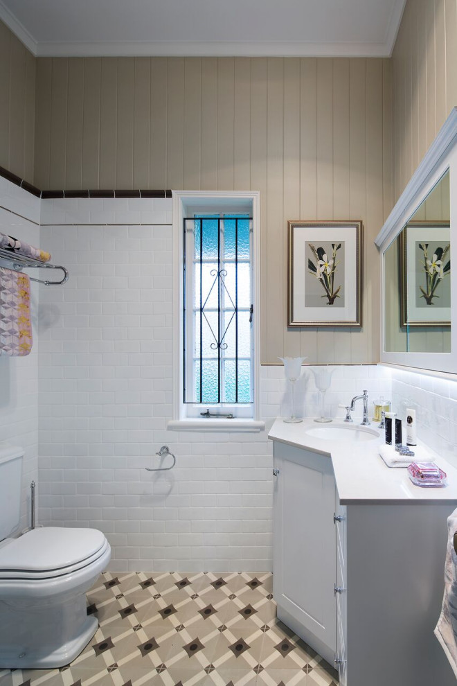 Klassisk inredning av ett litet vit vitt badrum, med vita skåp, en kantlös dusch, vit kakel, porslinskakel, ett undermonterad handfat, bänkskiva i kvarts och dusch med gångjärnsdörr