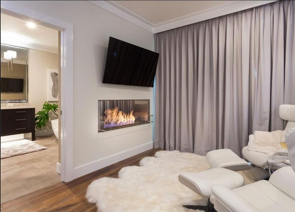 Photo of an expansive contemporary master bedroom in Tampa with white walls, medium hardwood floors, a two-sided fireplace and brown floor.