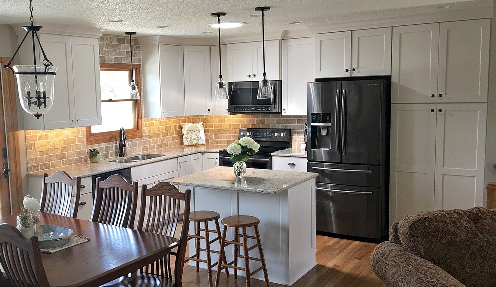 Inspiration for a mid-sized transitional l-shaped medium tone wood floor eat-in kitchen remodel with a double-bowl sink, shaker cabinets, white cabinets, granite countertops, beige backsplash, stone tile backsplash, black appliances and an island