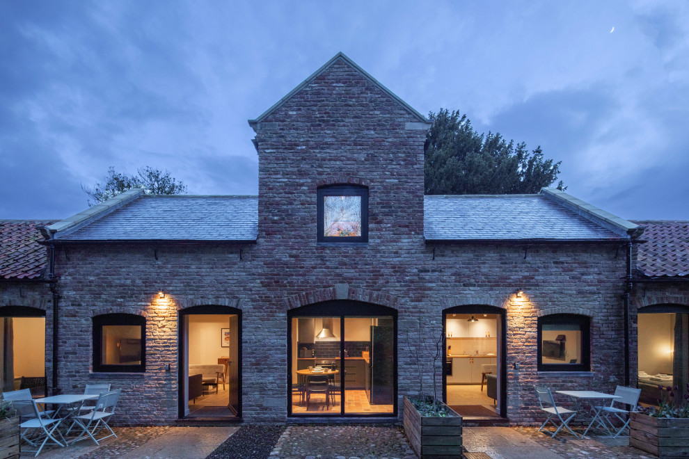 Réalisation d'une petite façade de Tiny House rouge champêtre en brique à un étage avec un toit à deux pans, un toit en tuile et un toit gris.
