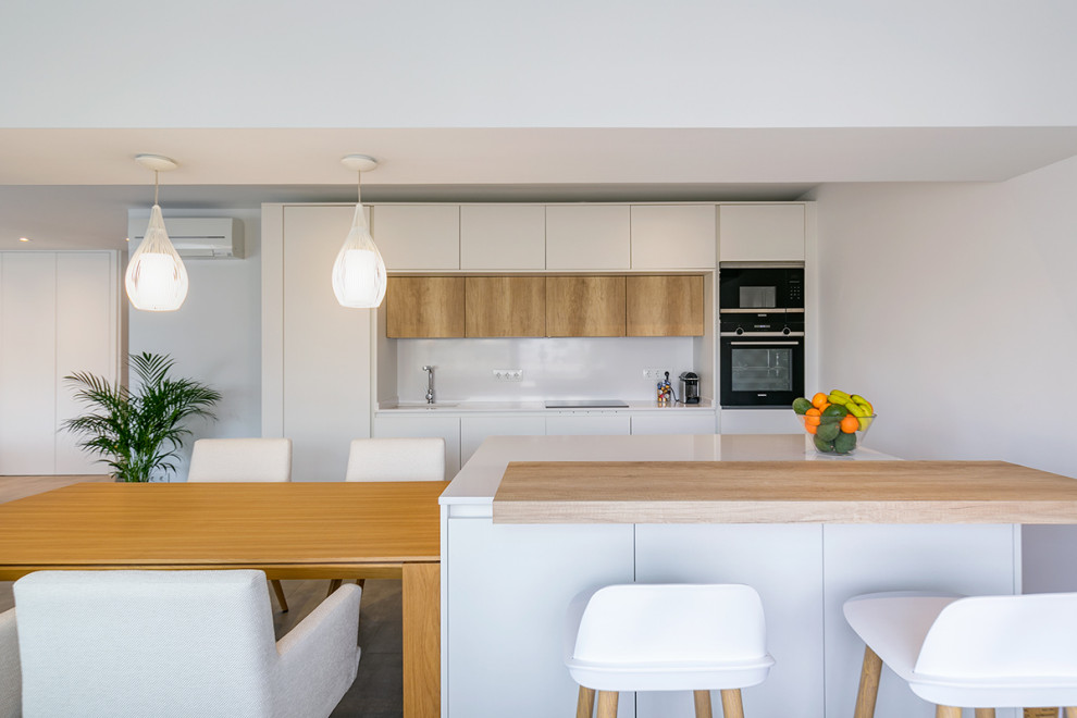 This is an example of a mid-sized modern single-wall open plan kitchen in Madrid with white cabinets, white splashback, black appliances, ceramic floors, multiple islands, grey floor and white benchtop.