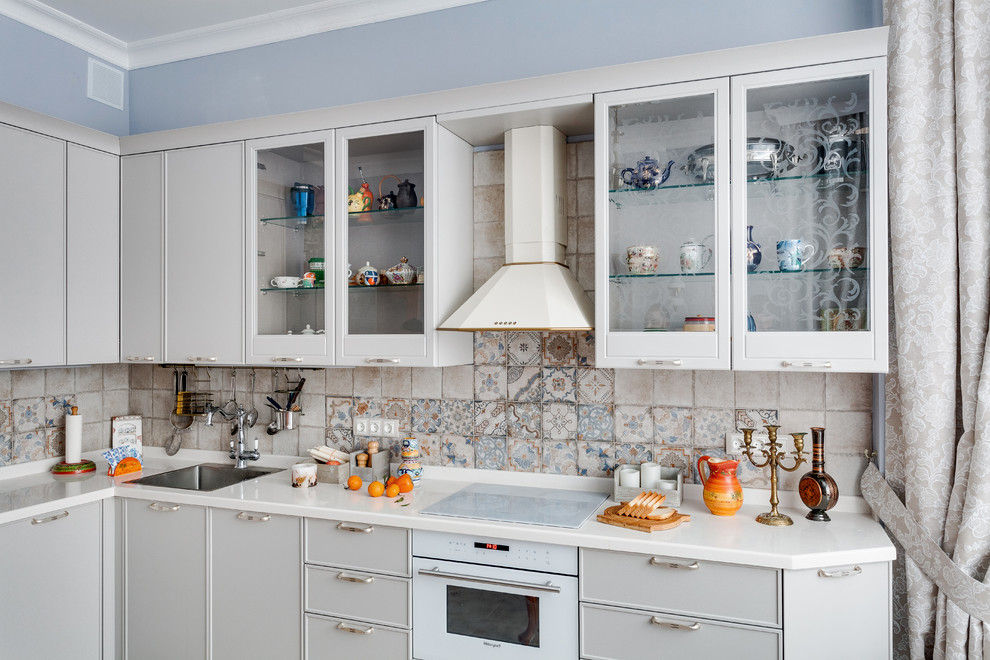 Design ideas for a large transitional l-shaped eat-in kitchen in Moscow with grey cabinets, ceramic splashback, white appliances, white benchtop, multi-coloured splashback, an undermount sink, glass-front cabinets, solid surface benchtops, ceramic floors and orange floor.