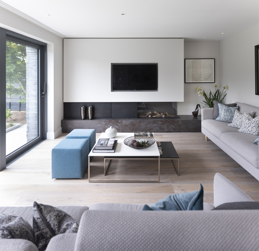 This is an example of a mid-sized modern enclosed living room in Cheshire with white walls, light hardwood floors, a ribbon fireplace, a metal fireplace surround, a built-in media wall and beige floor.