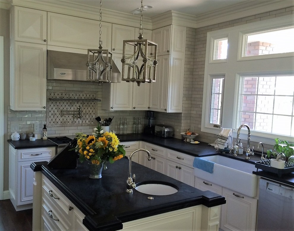 Mid-sized transitional l-shaped eat-in kitchen photo in San Francisco with a farmhouse sink, raised-panel cabinets, white cabinets, soapstone countertops, gray backsplash, subway tile backsplash, an island and black countertops