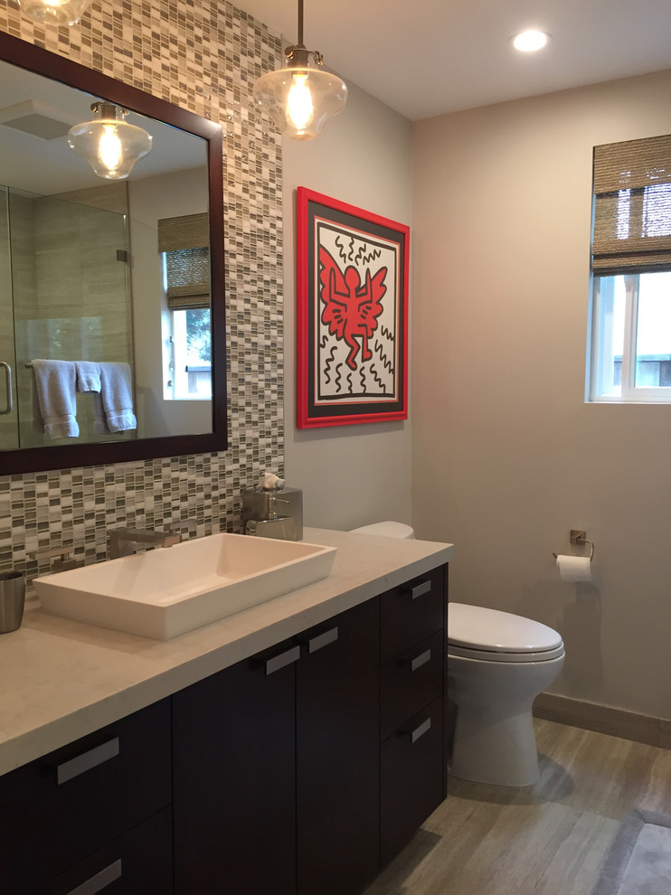 This is an example of a small contemporary bathroom in Los Angeles with flat-panel cabinets, brown cabinets, an alcove tub, a shower/bathtub combo, a one-piece toilet, gray tile, stone tile, grey walls, limestone floors, a vessel sink, engineered quartz benchtops, grey floor and a hinged shower door.