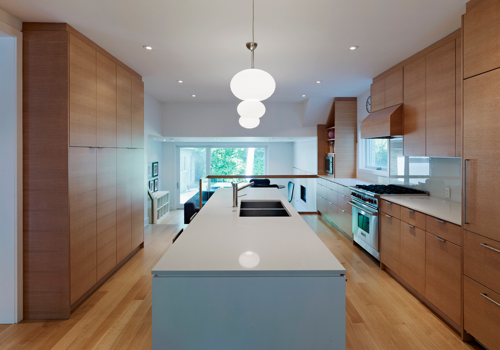 Design ideas for a large contemporary galley eat-in kitchen in Toronto with a double-bowl sink, flat-panel cabinets, medium wood cabinets, white splashback, glass sheet splashback, panelled appliances, light hardwood floors and with island.