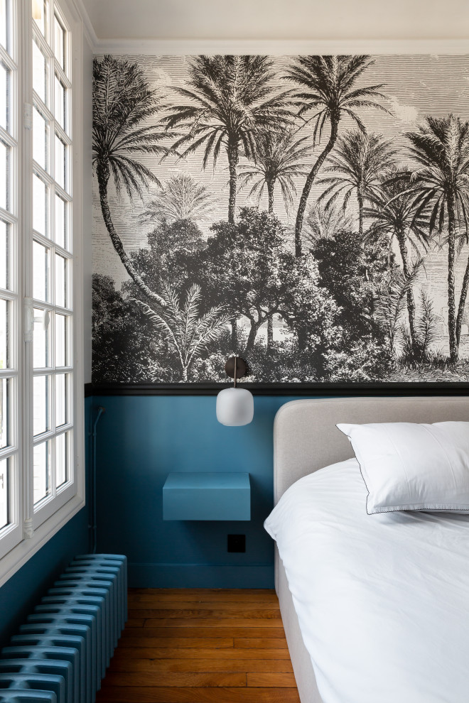 Großes Hauptschlafzimmer mit blauer Wandfarbe, hellem Holzboden, Kamin, Kaminumrandung aus Stein, braunem Boden und Tapetenwänden in Paris