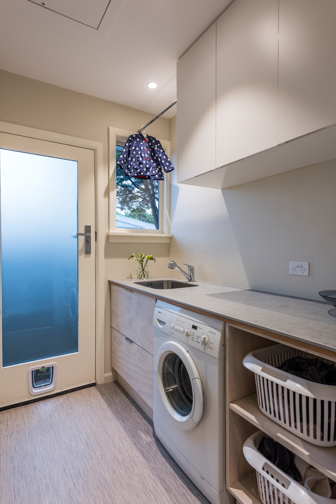 Photo of a contemporary single-wall dedicated laundry room in Other with an undermount sink, light wood cabinets and vinyl floors.