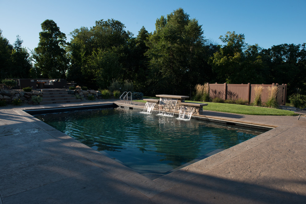 Photo of a mid-sized contemporary backyard rectangular pool in Cedar Rapids with a water feature and stamped concrete.