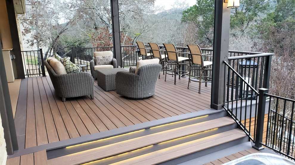 Photo of a large country backyard and first floor deck in Austin with a roof extension and metal railing.