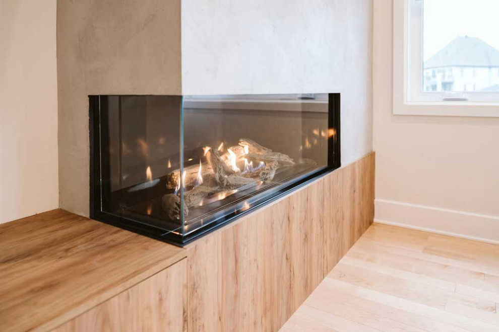 Diseño de salón abierto minimalista grande con paredes beige, suelo de madera clara, chimenea de esquina, marco de chimenea de hormigón y televisor colgado en la pared
