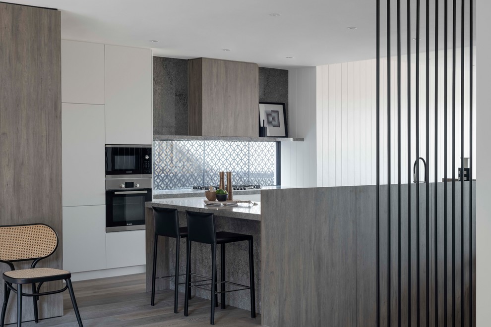 This is an example of a large contemporary eat-in kitchen in Sydney with a double-bowl sink, flat-panel cabinets, white cabinets, quartz benchtops, glass sheet splashback, stainless steel appliances, medium hardwood floors, with island, brown floor and grey benchtop.