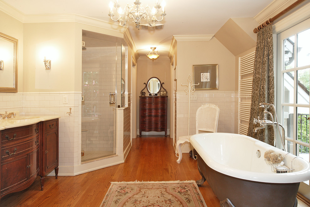 This is an example of a large traditional master bathroom in New York with brown cabinets, a claw-foot tub, an alcove shower, white tile, ceramic tile, dark hardwood floors, an undermount sink, engineered quartz benchtops, a hinged shower door, beige benchtops, an enclosed toilet, a double vanity, a freestanding vanity and furniture-like cabinets.