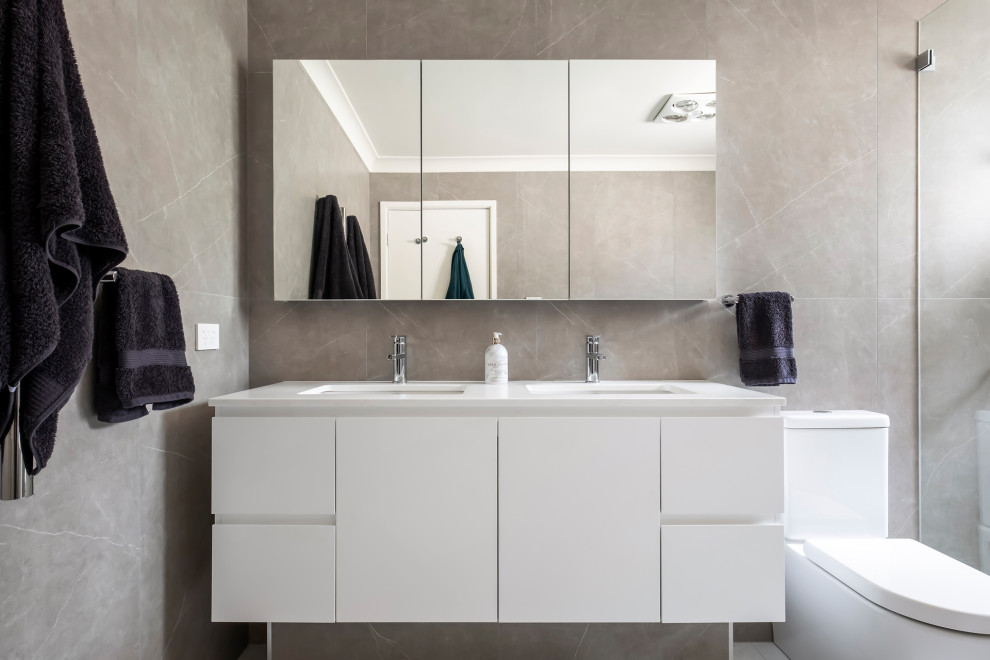 Design ideas for a mid-sized contemporary master bathroom in Sydney with flat-panel cabinets, white cabinets, a freestanding tub, an open shower, a one-piece toilet, gray tile, porcelain tile, grey walls, porcelain floors, an integrated sink, solid surface benchtops, white floor, an open shower, white benchtops, a niche, a double vanity and a freestanding vanity.