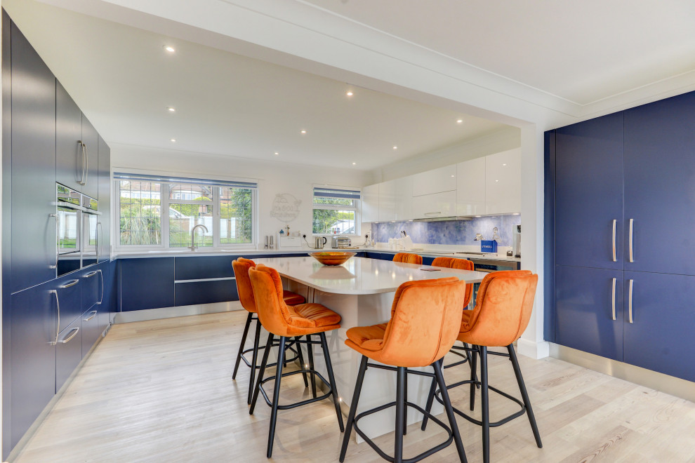Inspiration for a large contemporary u-shaped open plan kitchen in Sussex with an integrated sink, flat-panel cabinets, blue cabinets, quartzite benchtops, blue splashback, glass sheet splashback, panelled appliances, vinyl floors, with island, brown floor and white benchtop.