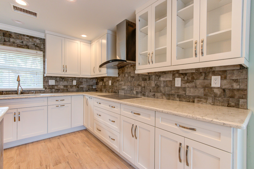 Large transitional u-shaped porcelain tile and brown floor enclosed kitchen photo with an undermount sink, shaker cabinets, white cabinets, quartz countertops, brown backsplash, stainless steel appliances, an island and beige countertops