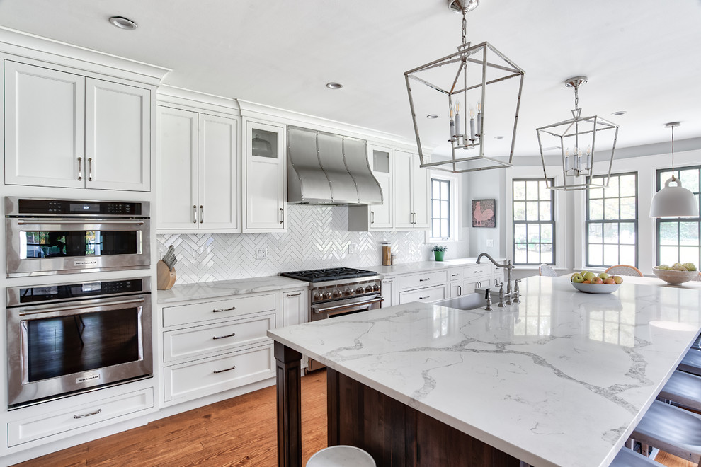 Expansive traditional galley eat-in kitchen in New York with a farmhouse sink, beaded inset cabinets, white cabinets, quartzite benchtops, white splashback, subway tile splashback, stainless steel appliances, medium hardwood floors, with island and white benchtop.