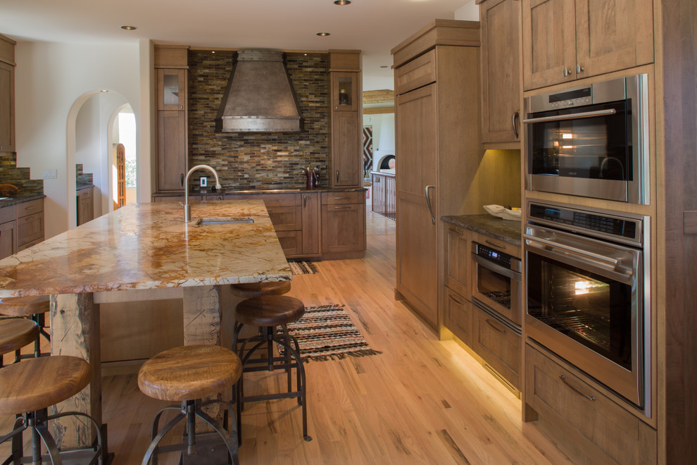 Large country u-shaped open plan kitchen in Calgary with a single-bowl sink, shaker cabinets, medium wood cabinets, granite benchtops, multi-coloured splashback, matchstick tile splashback, panelled appliances, light hardwood floors and with island.
