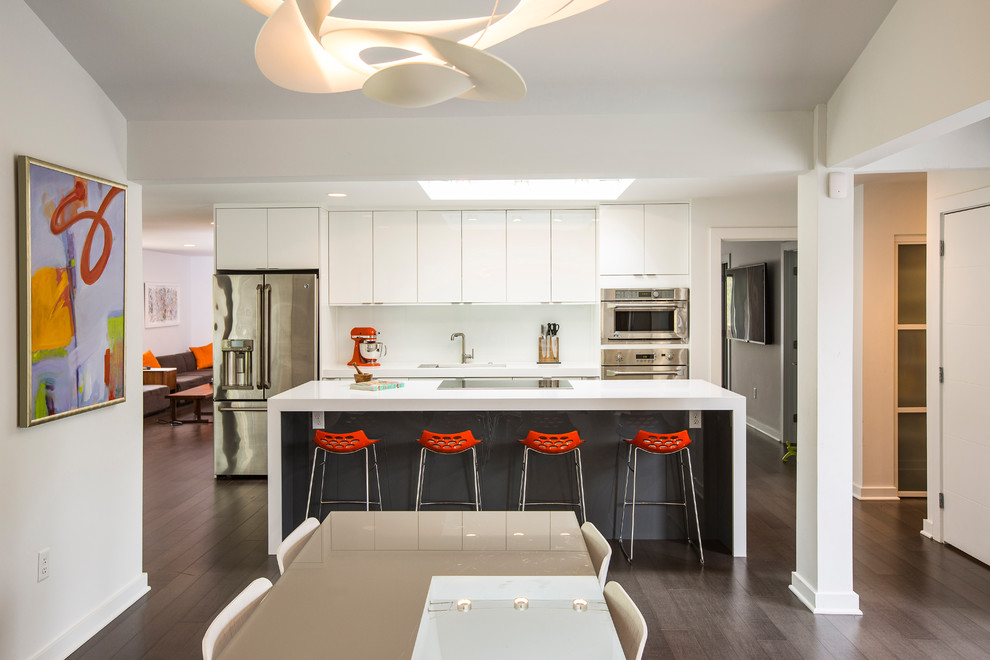 Photo of a mid-sized modern single-wall eat-in kitchen in Cincinnati with an undermount sink, flat-panel cabinets, white cabinets, solid surface benchtops, stainless steel appliances, dark hardwood floors, with island, brown floor and white benchtop.
